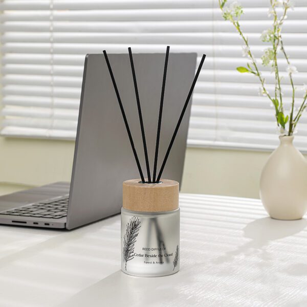 rosted reed diffuser with wood cap and black sticks on white table