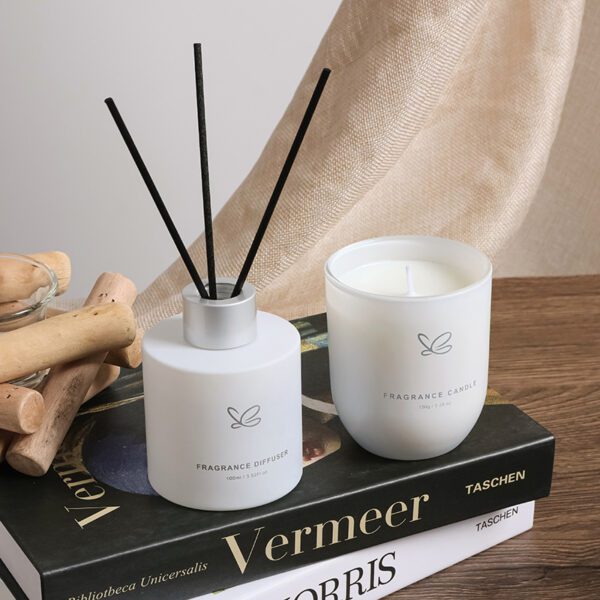 Close-up of frosted glass reed diffuser and white candle in minimalist packaging