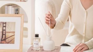 Reed diffuser how to use—hands placing reeds into a glass diffuser bottle on a tray.